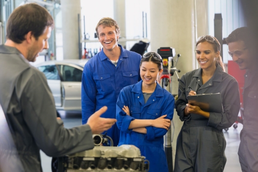 Eine Gruppe Auszubildende bekommt etwas Technisches an einem Motorblock erklärt.